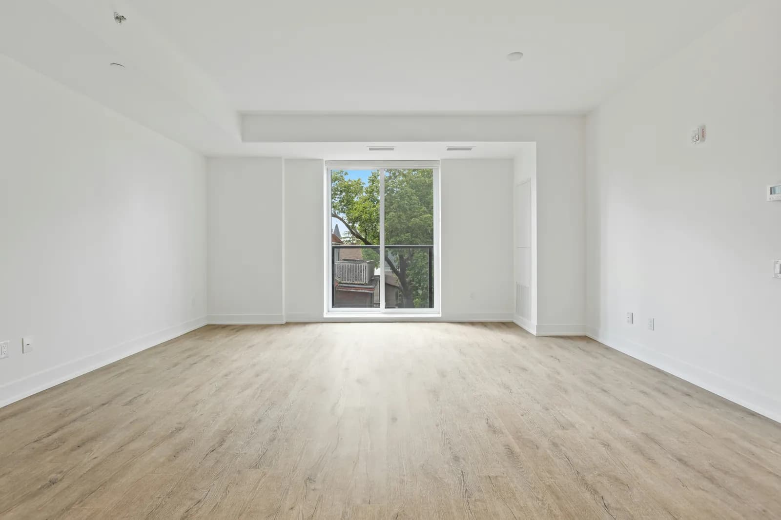 An empty living room with pale wood floors and a tall window